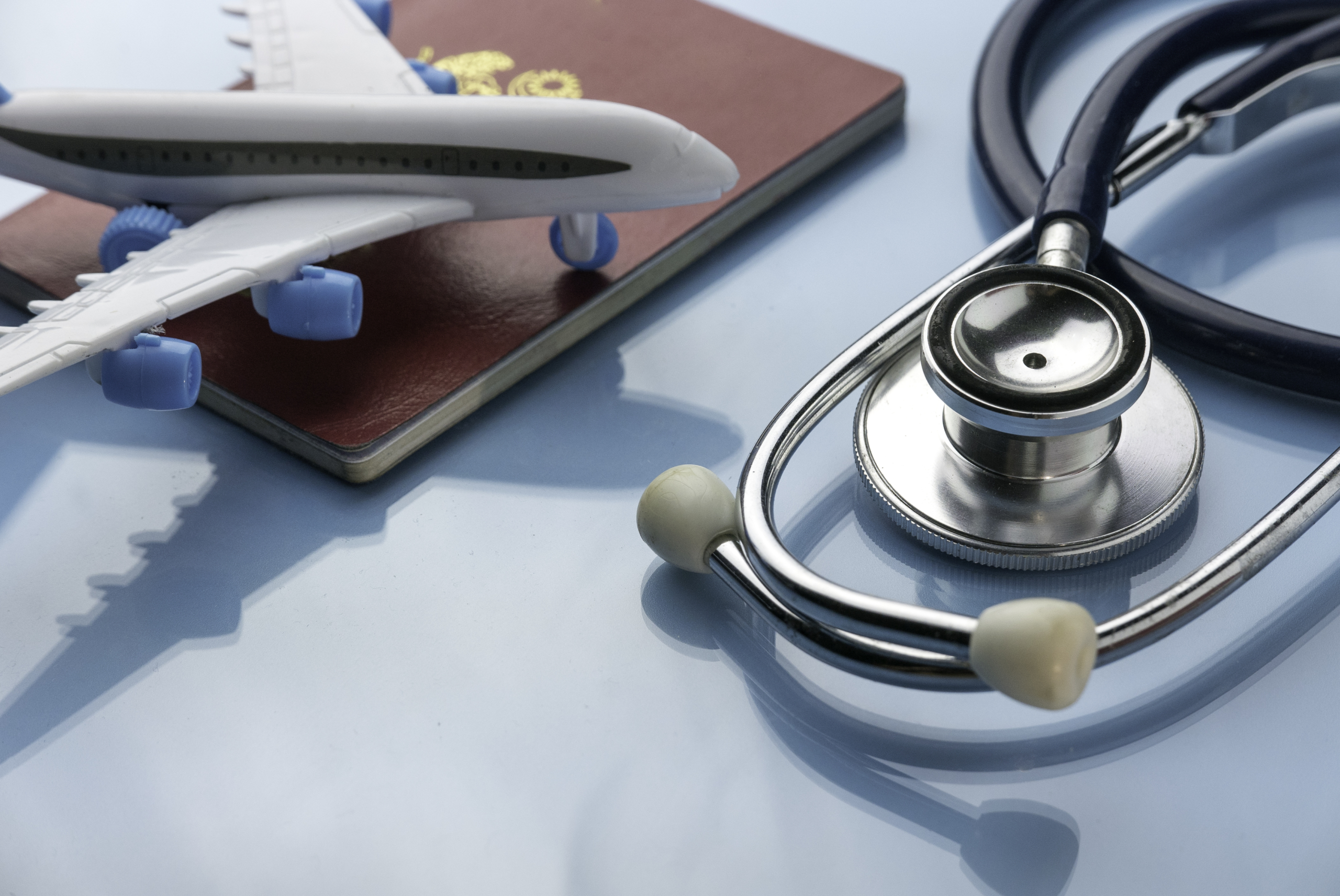 Healthcare,transportation and tourism concept with stethoscope, passport and plane model on a blue glass background.