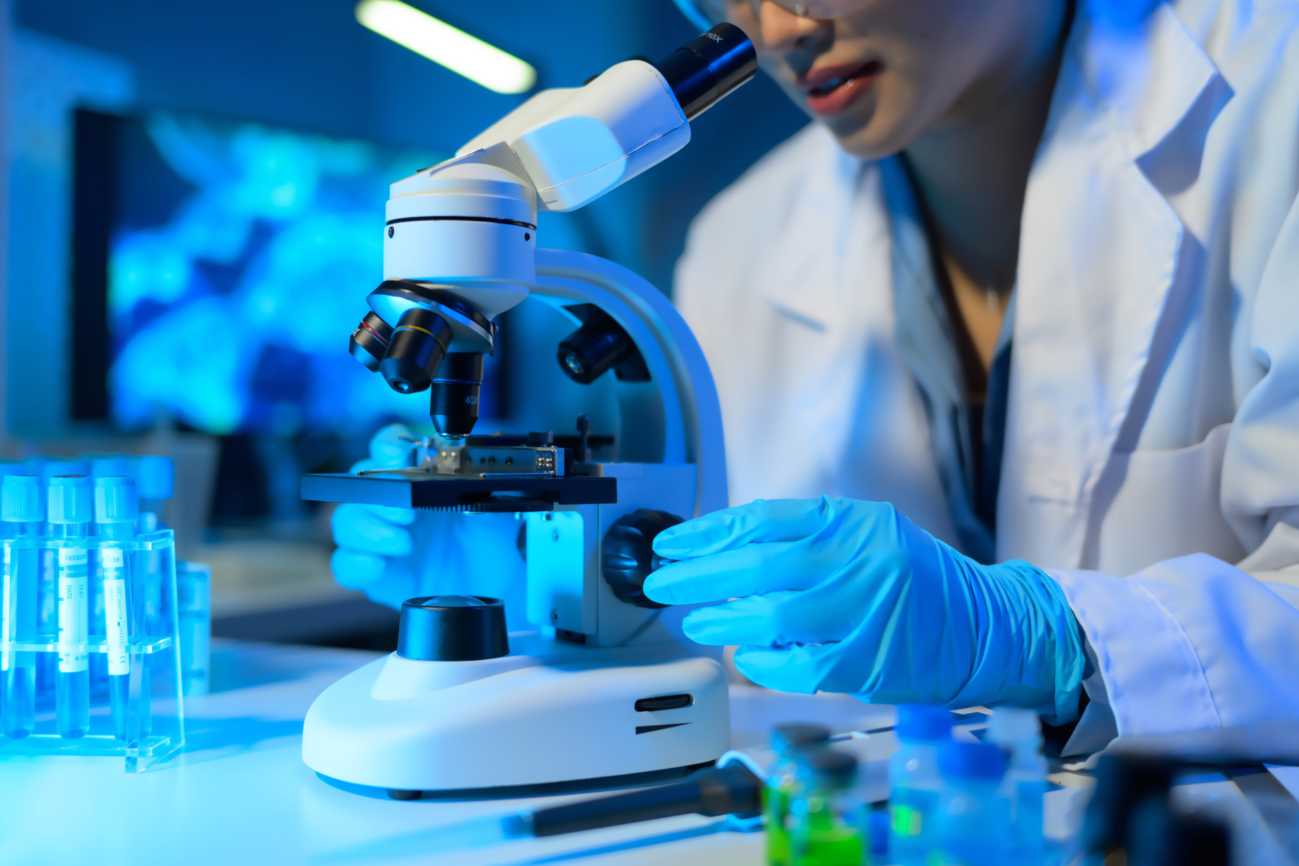 A woman in a lab coat is using a microscope to examine a sample